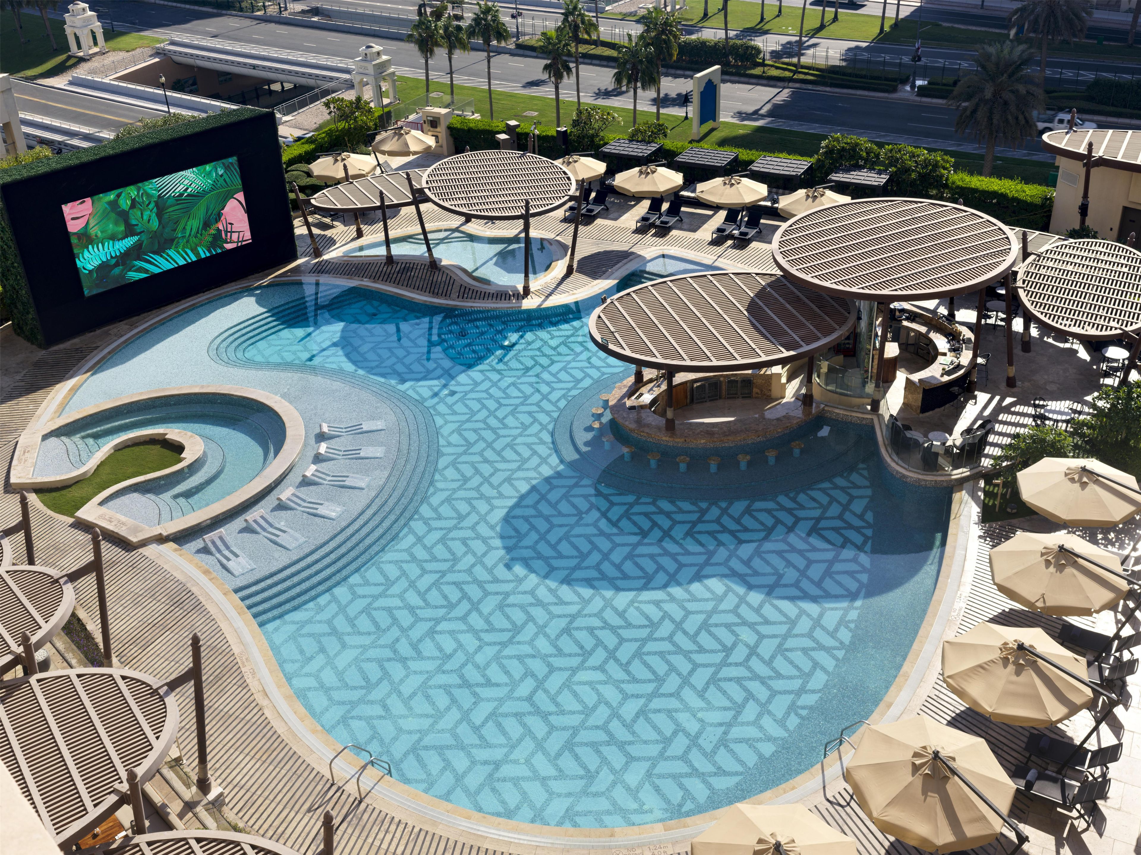 Uma piscina grande ao ar livre com várias áreas para banho de sol e um bar.