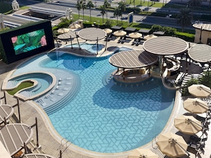 A large outdoor swimming pool with multiple sunbathing areas and a bar. - Hilton Doha The Pearl (Doha)