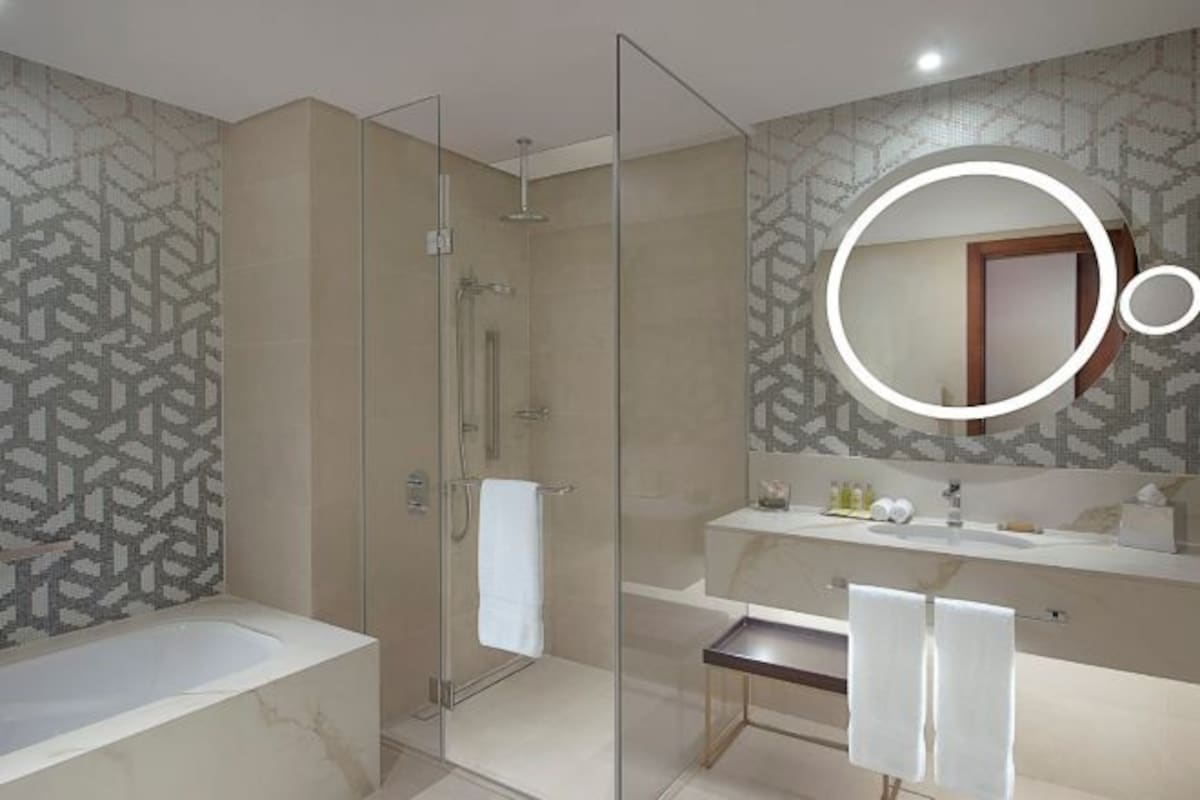 A modern bathroom with a glass-enclosed shower, a marble bathtub, and a vanity with a mirror.