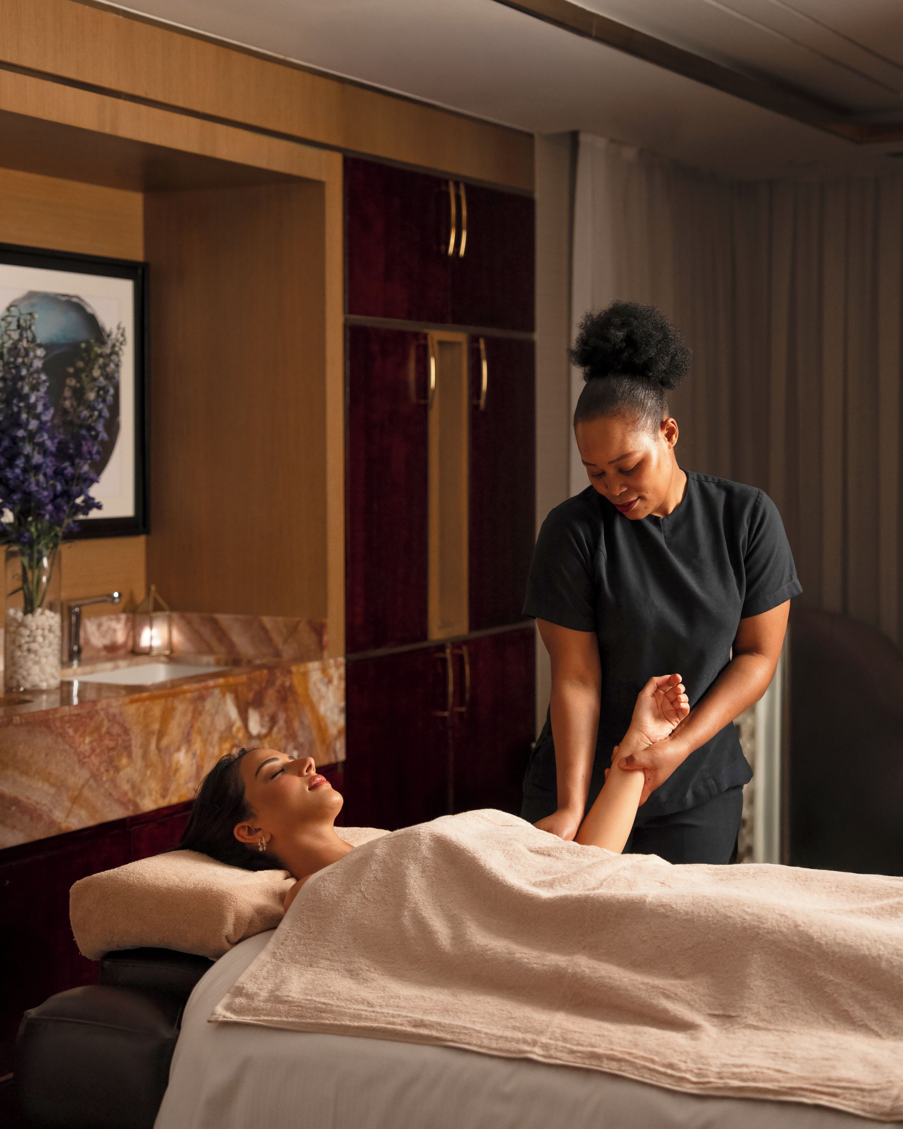 A massage therapy session in a room with a marble countertop, wooden cabinets, and a framed artwork on the wall.