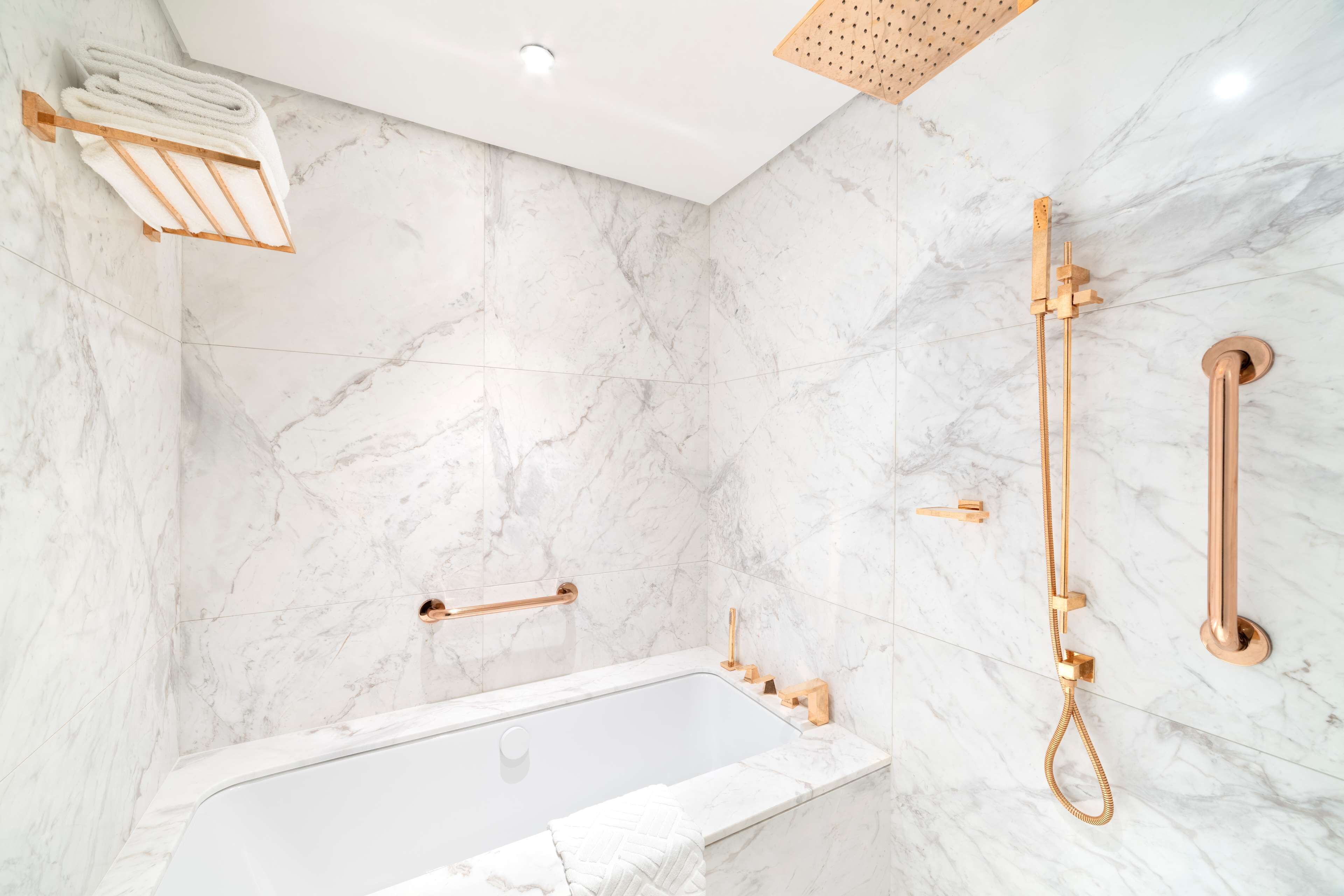 A modern bathroom with a marble wall, a bathtub, and a shower system.