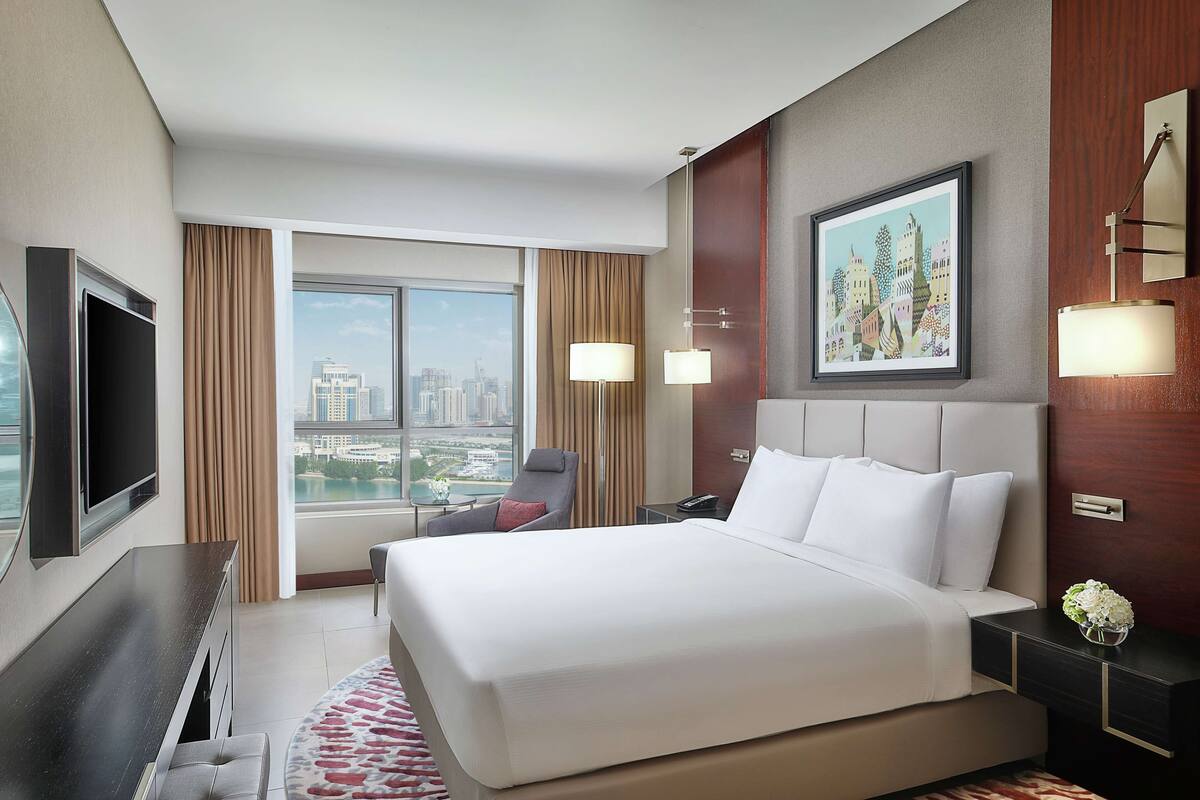 Une chambre d’hôtel moderne dotée d’un grand lit, d’une télévision à écran plat, d’un bureau et offrant une vue sur la ville.