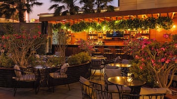 Un espace bar extérieur avec des tables et des chaises, entouré de plantes et de palmiers.