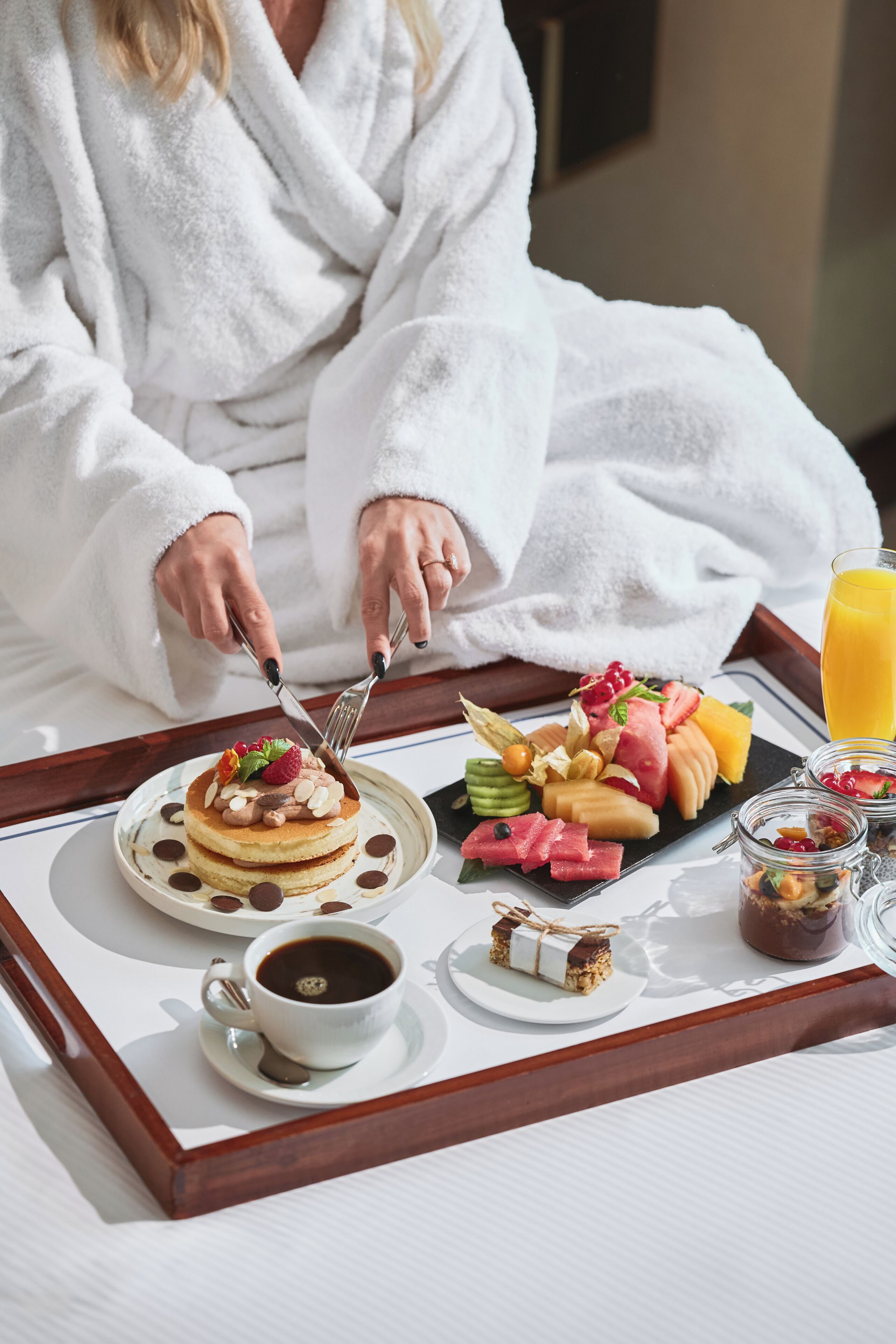 Un plateau de petit-déjeuner avec des crêpes, des fruits, une tasse de café et un verre de jus d’orange.