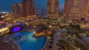 Zona de piscina de un resort con varias piscinas, sillones de descanso y un paseo bien iluminado.