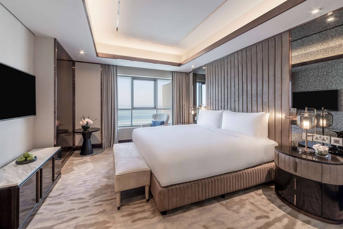 Une chambre d’hôtel moderne dotée d’un grand lit, d’un téléviseur à écran plat, d’une table de chevet, d’un petit bureau et offrant une vue sur la ville.