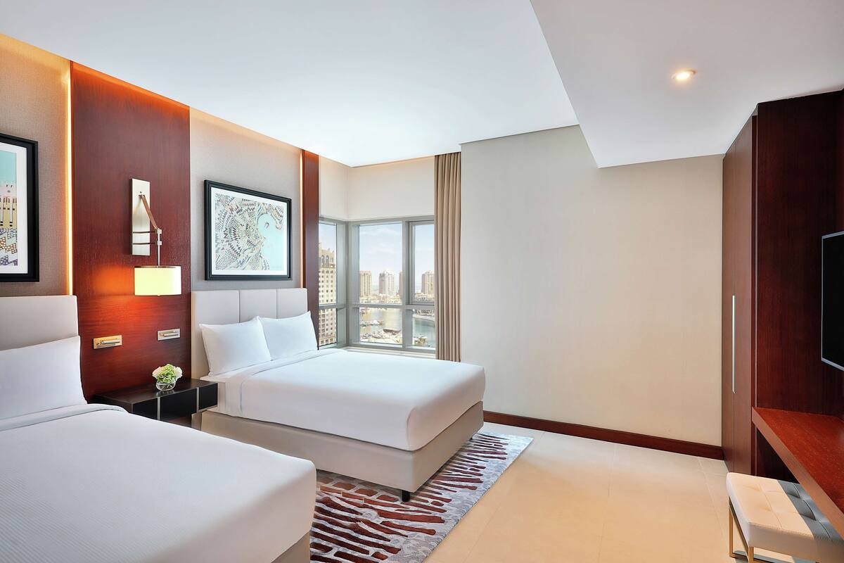 Une chambre d’hôtel avec deux lits, une grande fenêtre donnant sur la ville, un téléviseur à écran plat et un mur décoratif en bois.