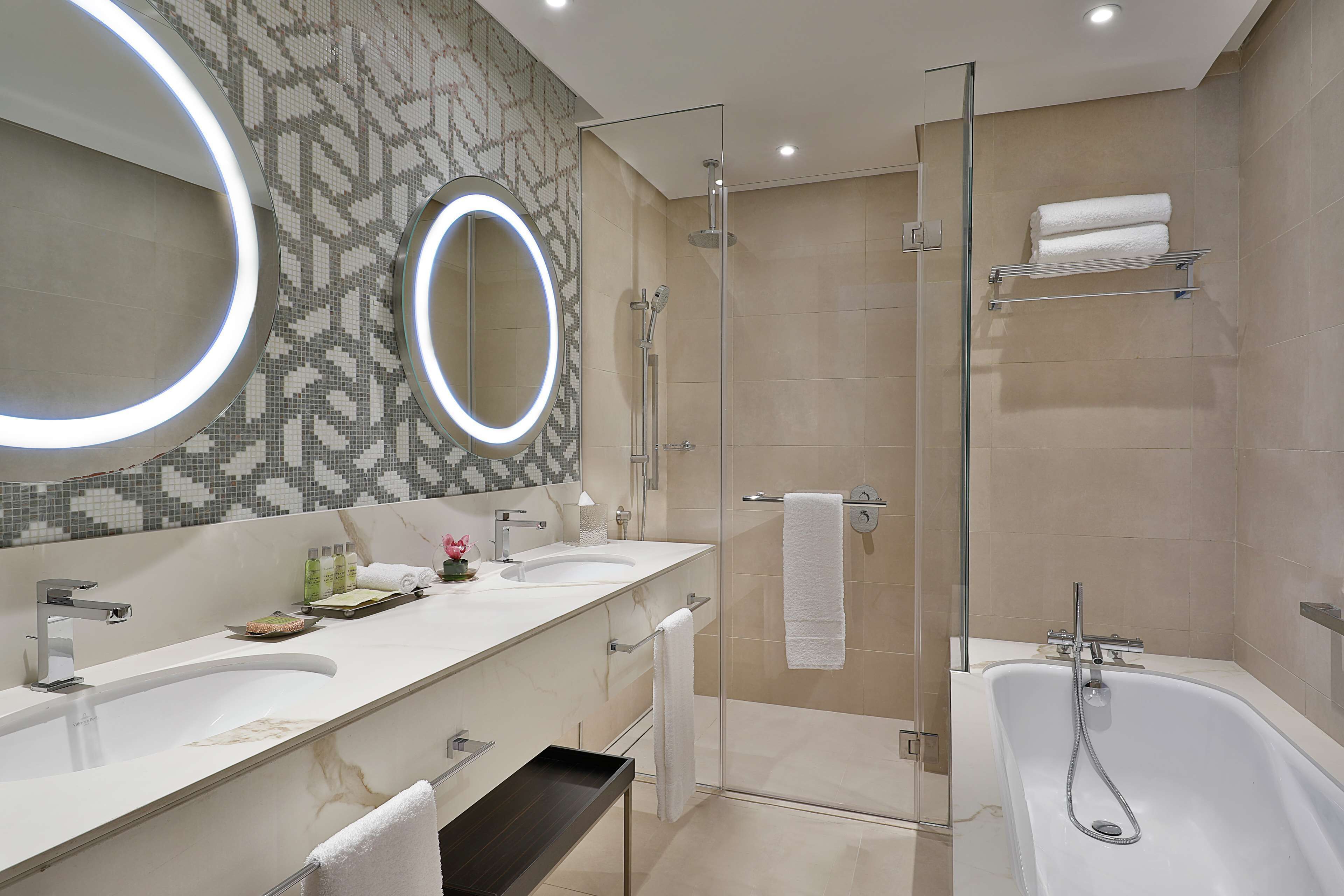 Ein modernes Badezimmer mit zwei Waschbecken, einer Duschkabine, einem großen Spiegel mit Beleuchtung und einer Badewanne.