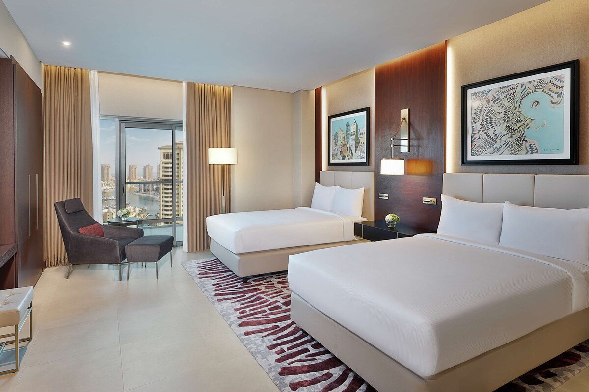 A hotel room with two beds, a sofa, a TV, and a view of the cityscape.