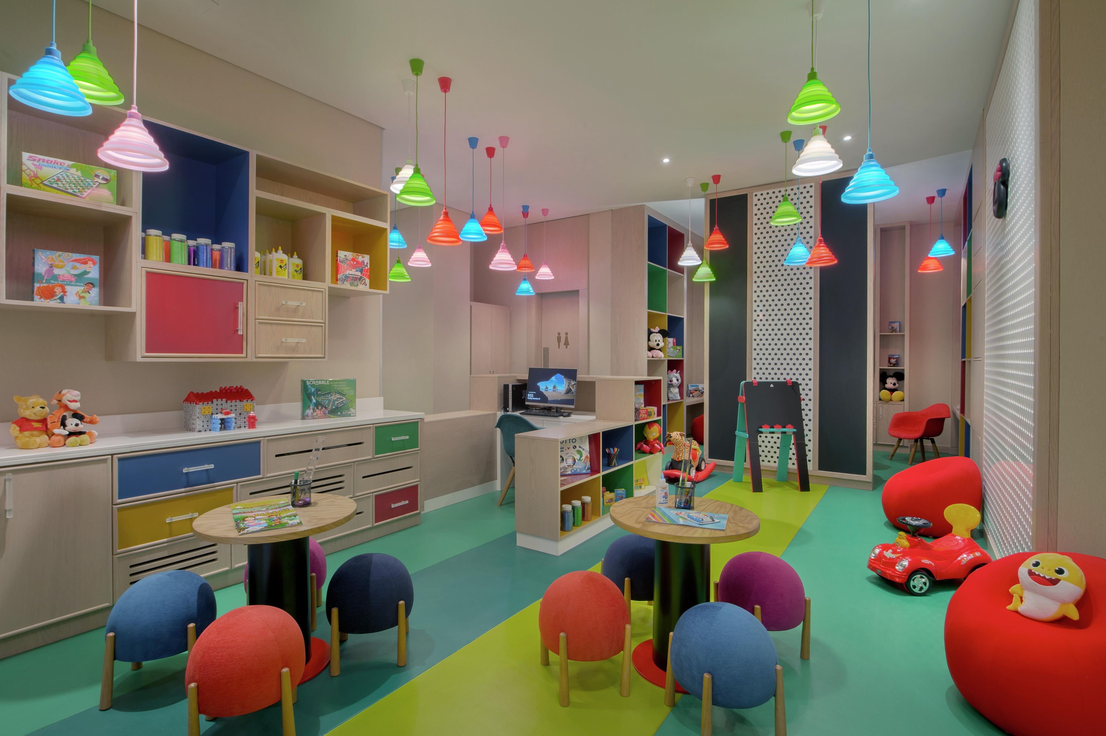 A children's playroom with colorful furniture, shelves with toys and books, and hanging multicolored lights.