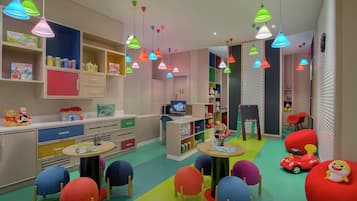 A children's playroom with colorful furniture, shelves with toys and books, and hanging multicolored lights.