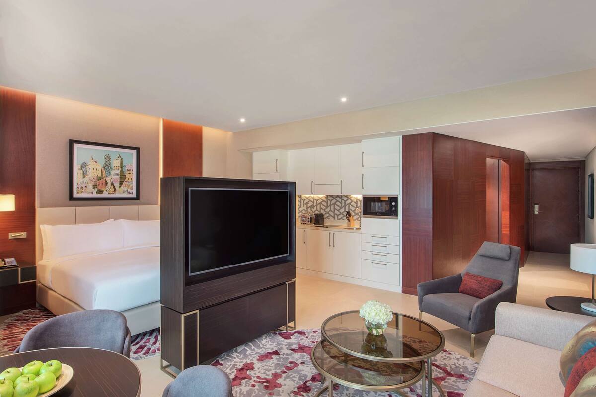 Une chambre d’hôtel avec un lit, une télévision, un coin salon avec une table basse et, au fond, une petite cuisine.