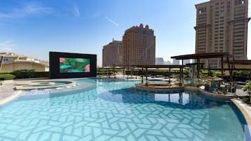 A swimming pool with a geometric tile pattern, surrounded by lounge areas and a large digital screen.