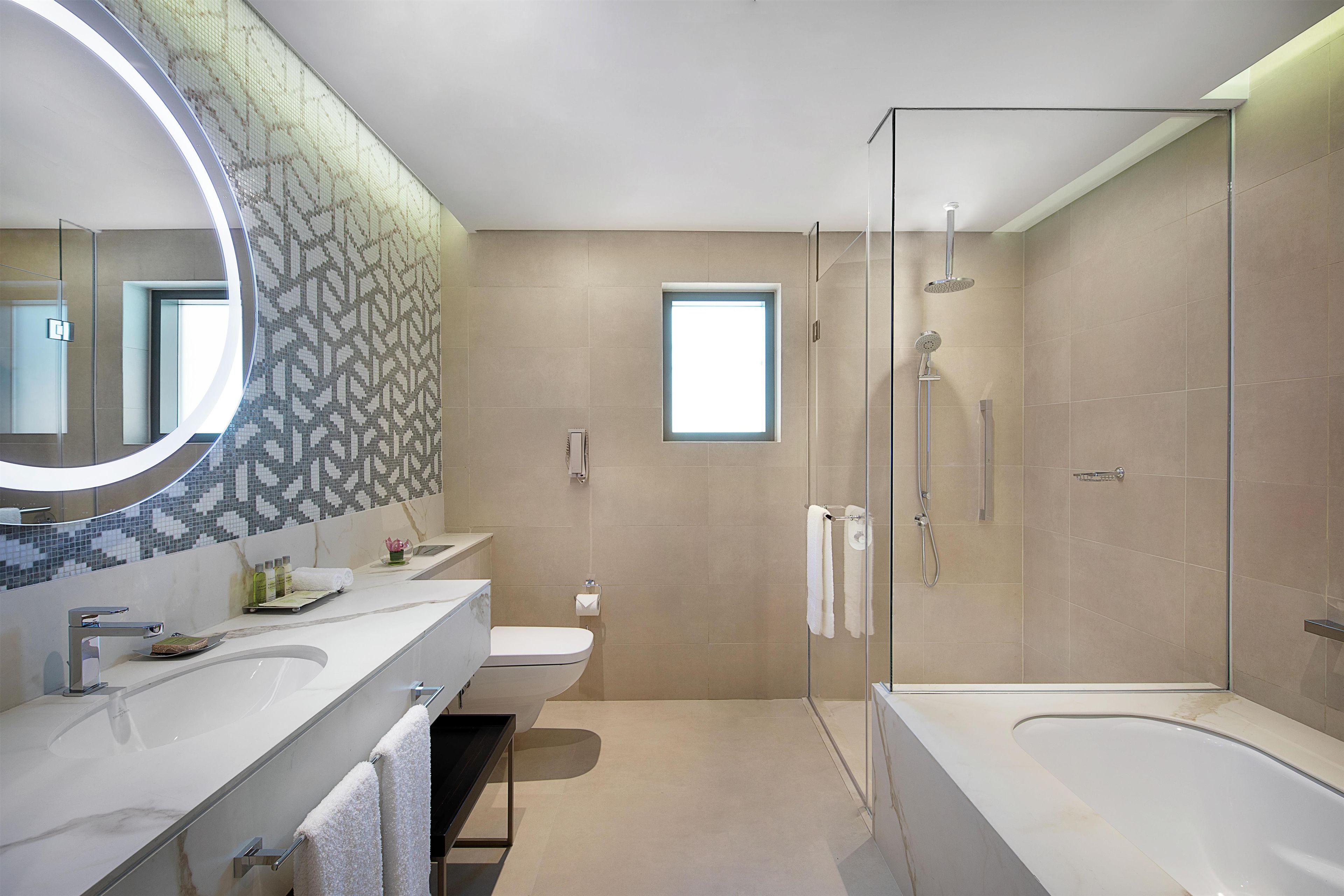 Une salle de bain moderne avec un grand miroir, deux lavabos, des toilettes et une baignoire.