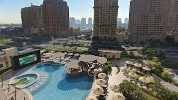 A resort with a large swimming pool, outdoor seating, and high-rise buildings in the background.