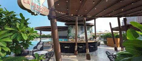 A poolside bar area with a sign reading "LA PERGOLA".