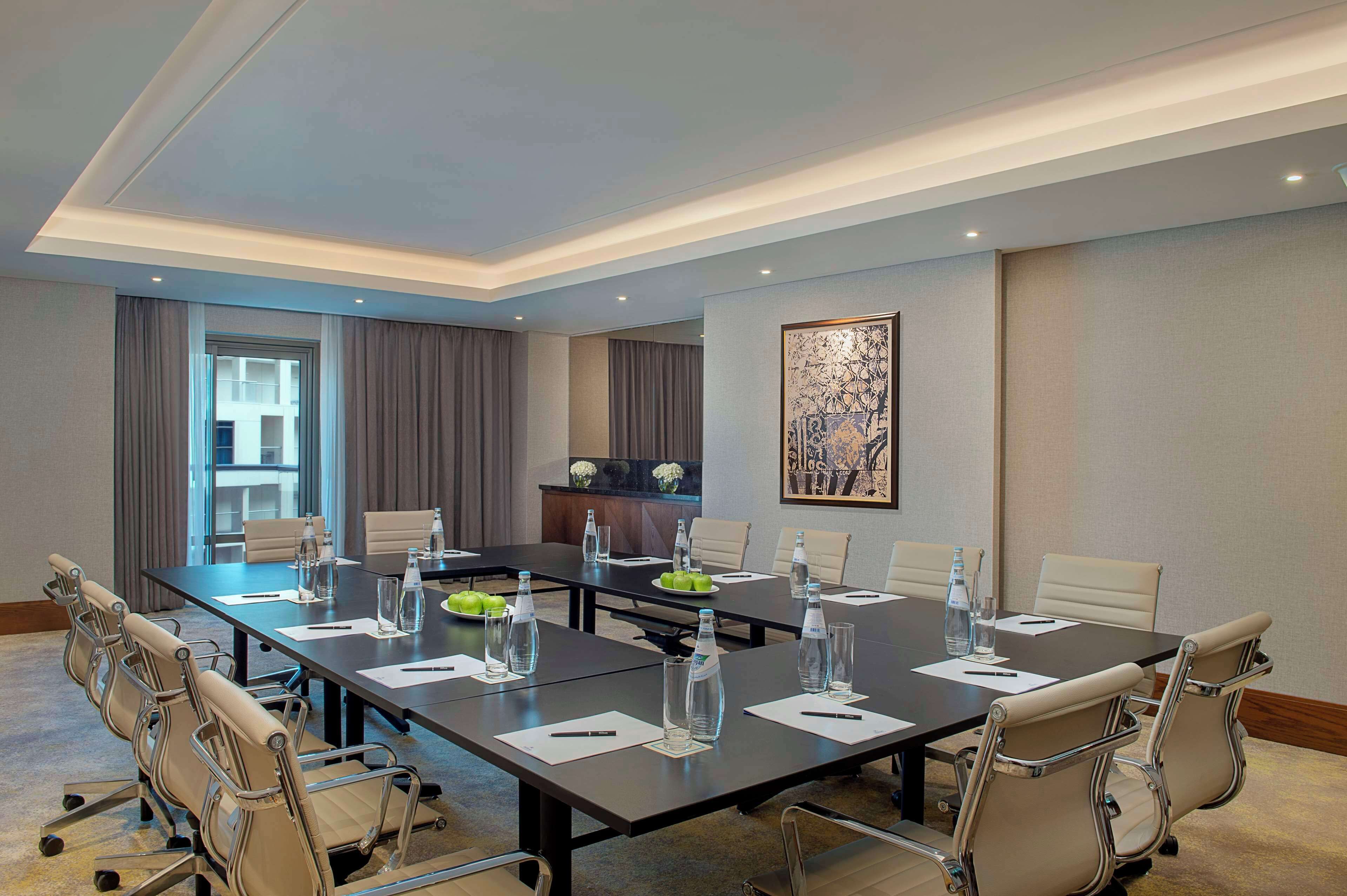 A conference room with a long table, chairs, water bottles, and a decorative piece on the wall.
