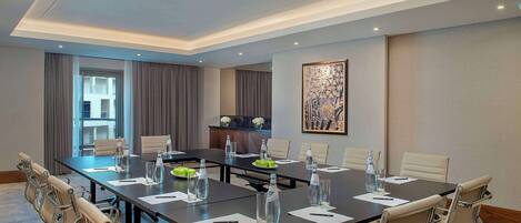 A conference room with a long table, chairs, water bottles, and a decorative piece on the wall.