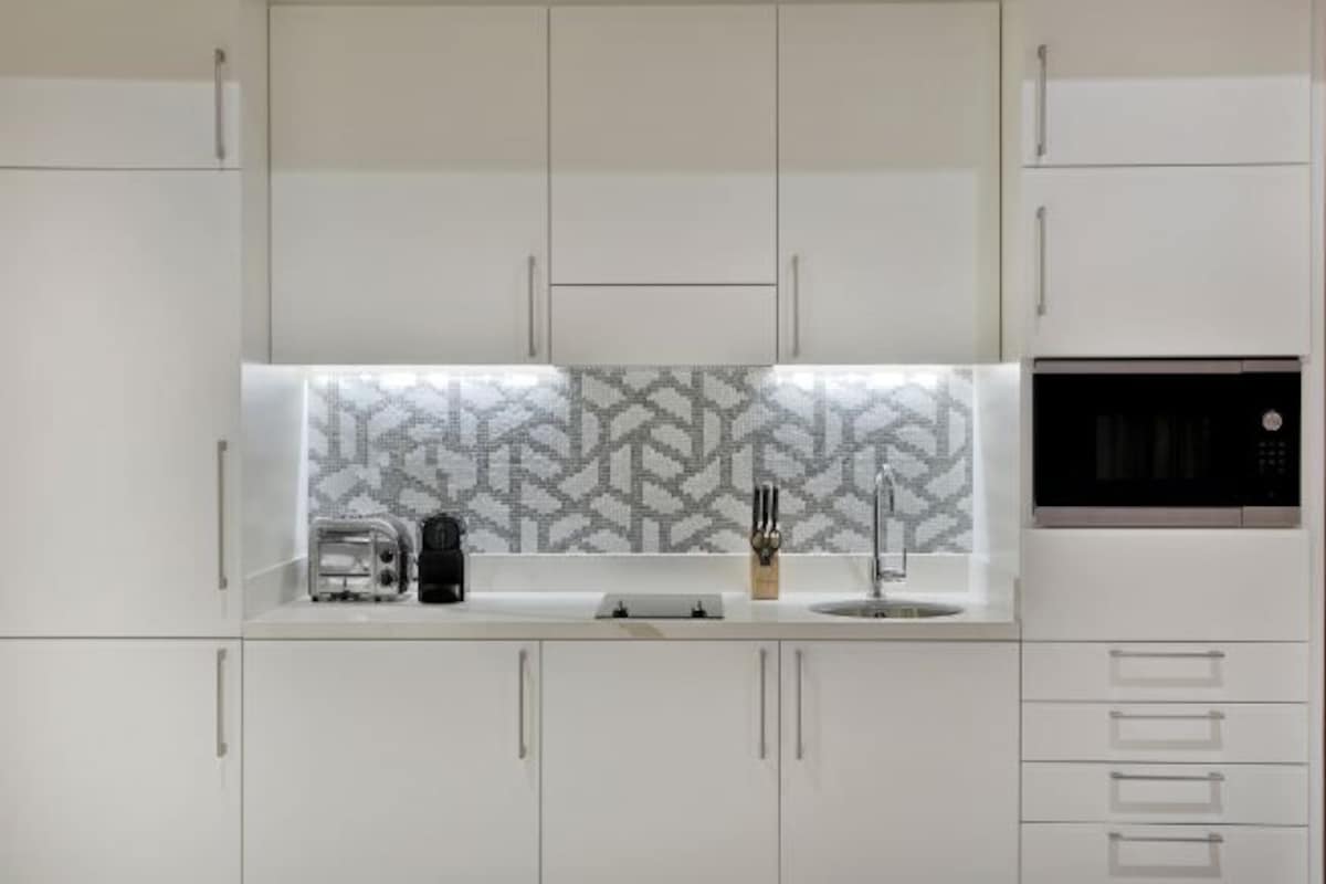 A modern kitchen with white cabinets, a patterned backsplash, a toaster, a coffee maker, and a microwave.