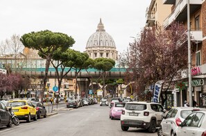A street view with parked cars, a large building with a dome, and a pedestrian overpass.