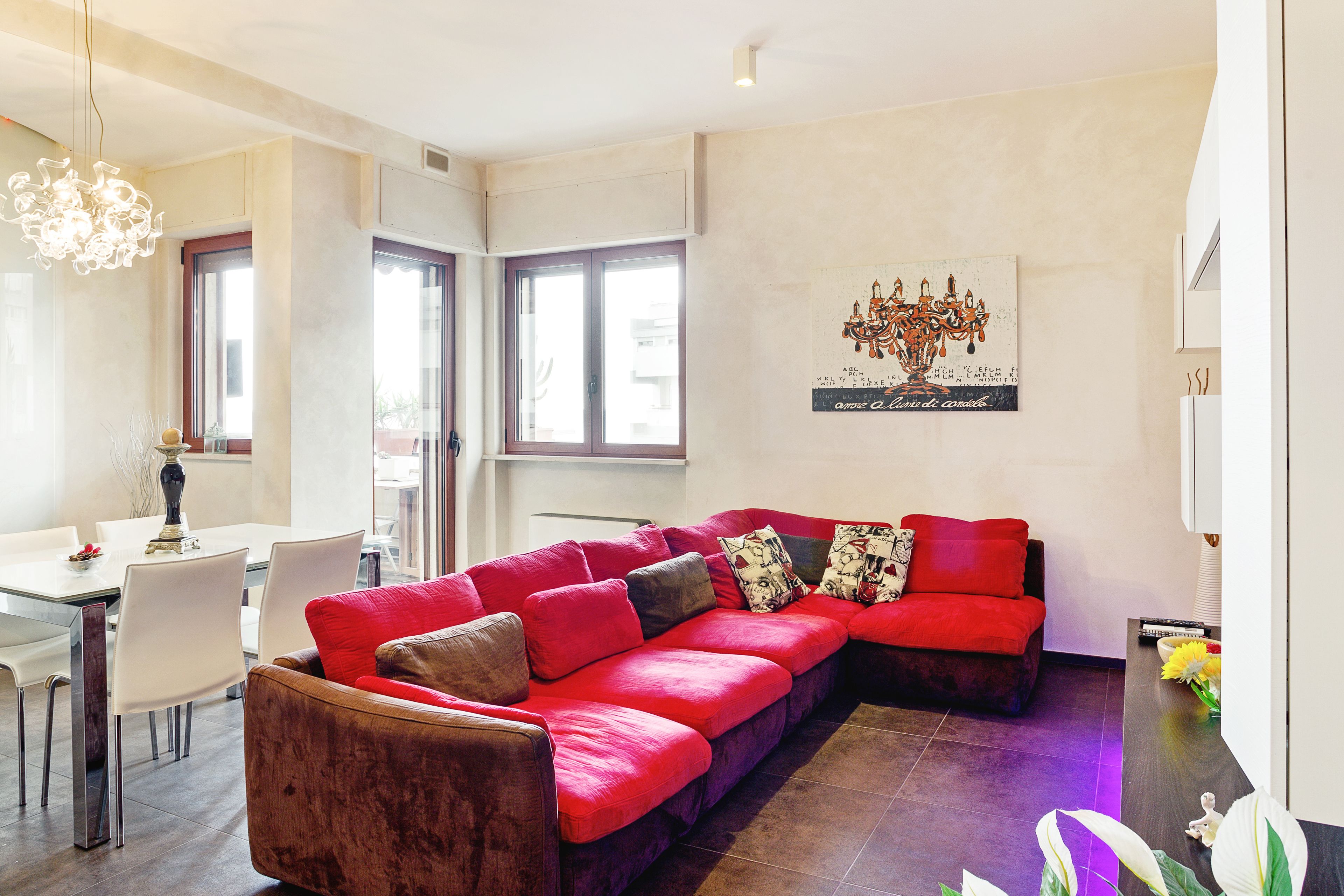 A modern living room with a red sectional sofa, a dining area with white chairs, and a large window providing natural light.
