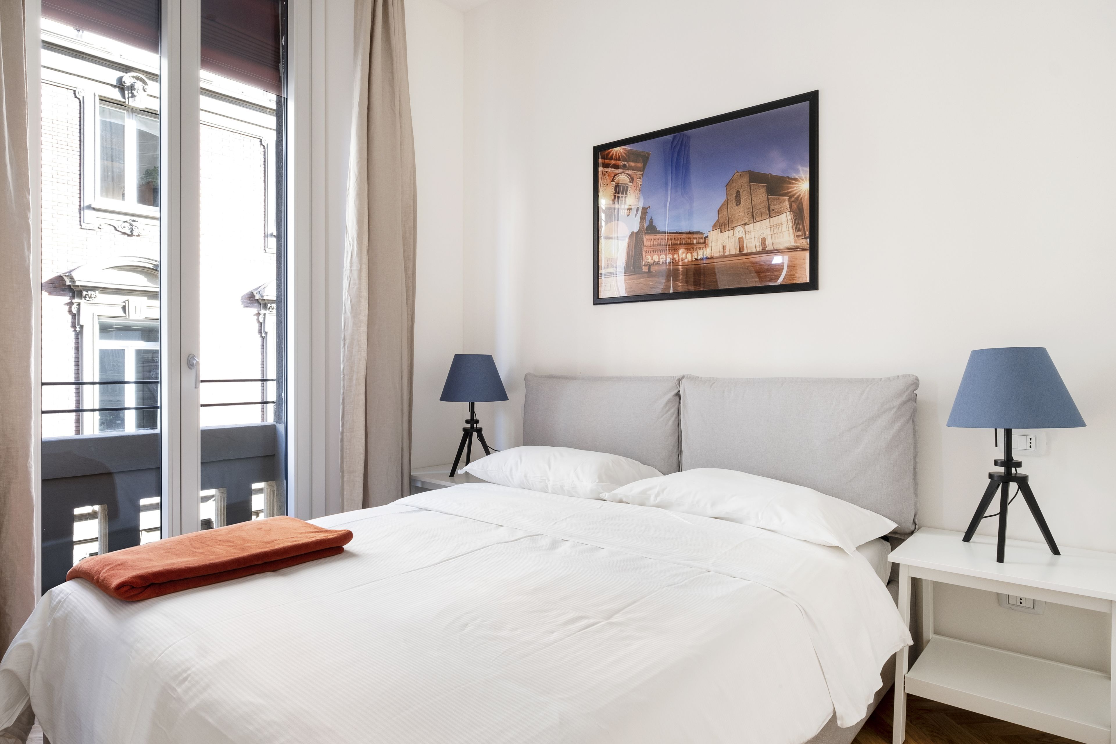 Une chambre d’hôtel avec un lit, deux lampes de chevet, un tableau encadré au mur et une fenêtre avec des rideaux.
