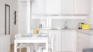 A modern kitchen with white cabinetry, a dining table with chairs, a coffee maker, and a fruit bowl.