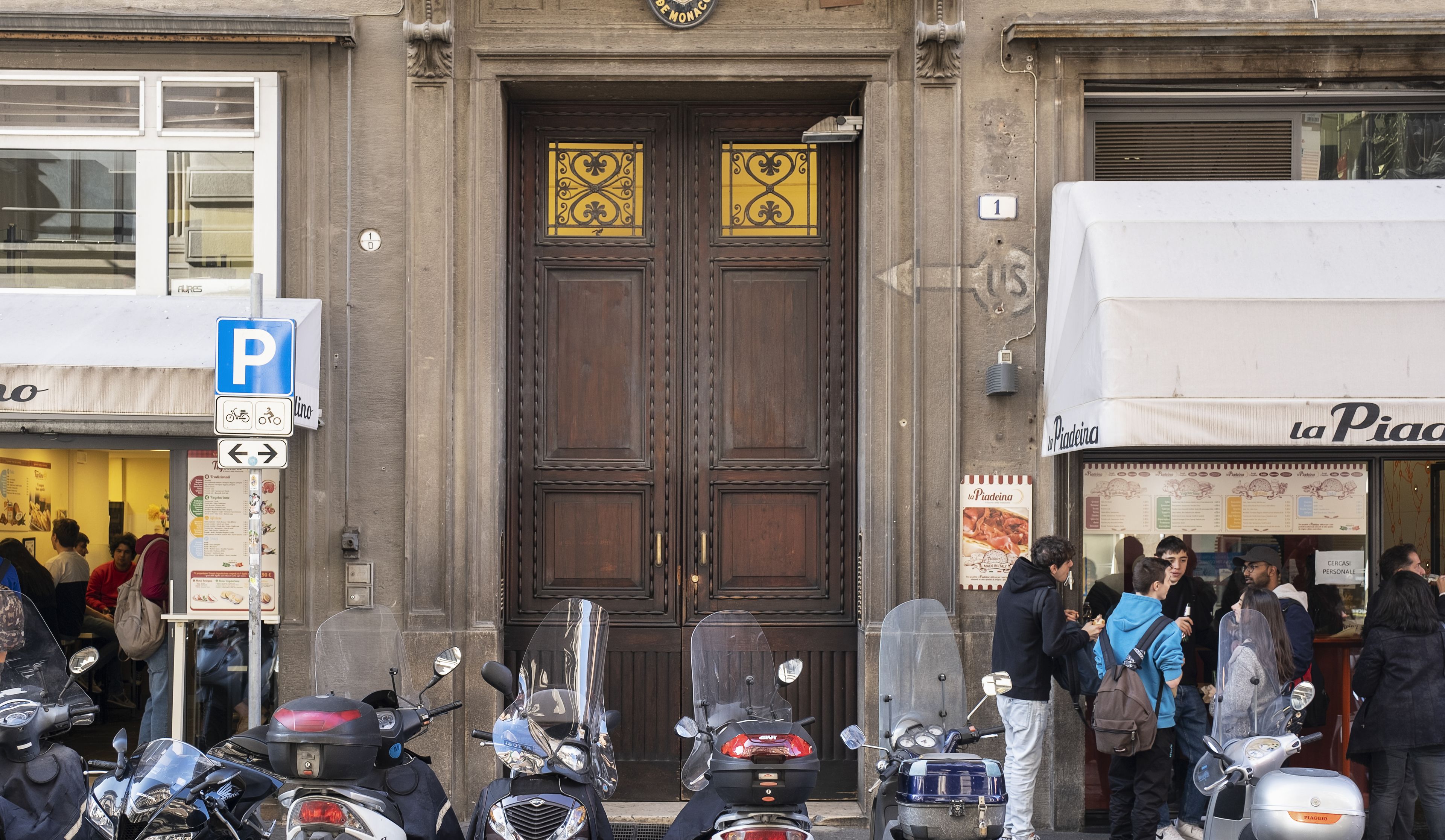 A building with a double wooden door, a sign indicating a parking area, and several parked scooters.