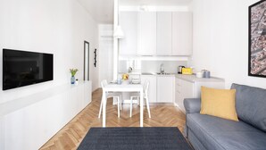 A modern apartment with a dining area, kitchenette, and a living room with a sofa and a TV.