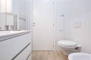 Et moderne badeværelse med toilet, bruseområde og et håndvaskarrangement med spejl og to vaser.