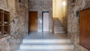 A marble-floored staircase leading to an elevator, with a red handrail and a wooden door on the left. - L'appartamento del Portico Mazzini (Bologna)