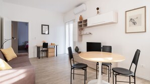 A modern living room with a sofa, a dining table with chairs, a TV, and a kitchen area with cabinets and a countertop. - L'appartamento del Portico Mazzini (Bologna)