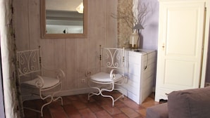 Een kamer met twee metalen stoelen, een witte ladekast, een spiegel en een deur.
