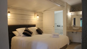 Een slaapkamer met een groot bed, nachtkastje, spiegel en een badkamer met wastafel en toilet.