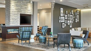 A modern lounge area with a stone fireplace, comfortable seating, and a wall decorated with framed pictures. - Residence Inn by Marriott Albany Airport (Albany)