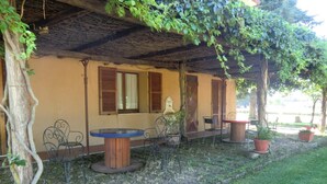 A rustic outdoor seating area with a round table and chairs, surrounded by potted plants and a thatched roof structure. - Agriturismo Cavallin del Bufalo (Manciano)