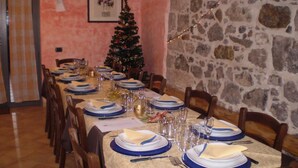 A long dining table set for a meal, with a Christmas tree and string lights in the background. - Agriturismo Cavallin del Bufalo (Manciano)