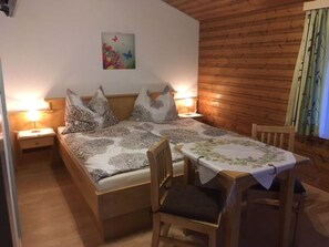 Ein Zimmer mit einem Bett, zwei Nachttischen, einem Sessel, einem Tisch mit Tischdecke und einer Holzwand.