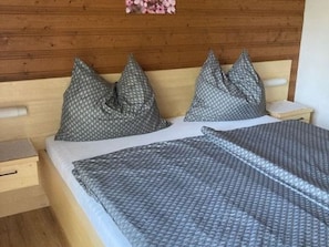 A bed with a patterned bedspread and two pillows, a wooden headboard, and a small bedside table with a drawer. - Double room 2 - Haus Bleckwand (Gschwendt)