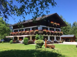 A traditional chalet with a balcony adorned with flowers, a well-maintained lawn, and a log structure in the foreground. - Double room 2 - Haus Bleckwand (Gschwendt)