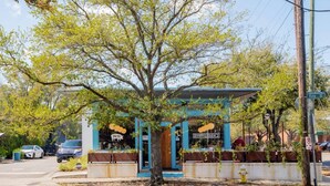 Un pequeño edificio de un piso con fachada azul, un cartel que dice 'RS' y un árbol en frente.