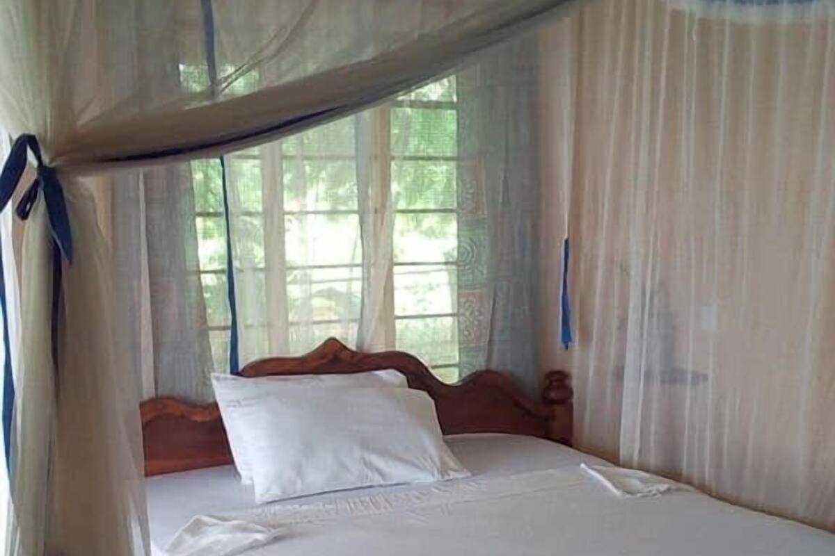 A single bed with a wooden frame and white bedding, covered by a mosquito net.