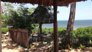 A rustic outdoor area with a thatched-roof structure, a wooden bench, and a view of the sea. - Chole Foxes lodge (Chole Island)