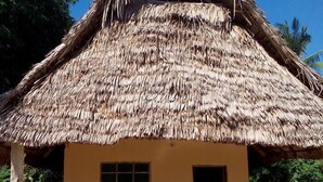 A thatched-roof hut with a simple, single-room layout, a bench outside, and a door leading to the interior. - Chole Foxes lodge (Chole Island)