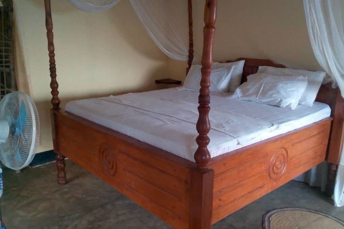 A four-poster bed with white bedding, a wooden frame, and a nightstand with a lamp.