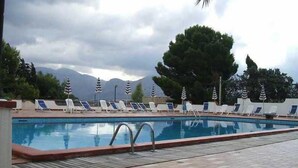 Une piscine entourée de chaises longues et de parasols, avec des arbres tout autour et des montagnes en arrière-plan.