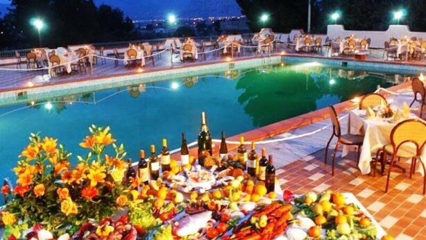 Un espace repas aménagé au bord de la piscine, avec des tables et des chaises, un buffet proposant divers plats, et une vue sur les montagnes en arrière-plan.