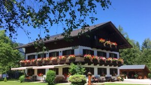 A traditional chalet with a balcony adorned with flowers, a well-maintained lawn, and a log structure in the foreground. - Double room 4 - Haus Bleckwand (Gschwendt)