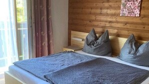 A bed with a grey blanket and pillows, wooden headboard, and a window with curtains. - Double room 4 - Haus Bleckwand (Gschwendt)