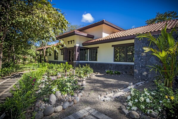Una casa moderna con fachada de piedra, amplios ventanales y un jardín cuidado con diversas plantas y un camino de grava.